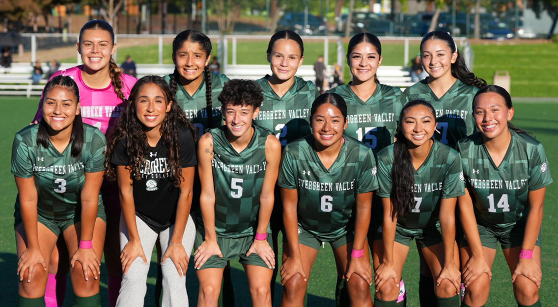 11 players in green jerseys and white numbers. one wearing pink goalie kit another wearing a black and white shirt.